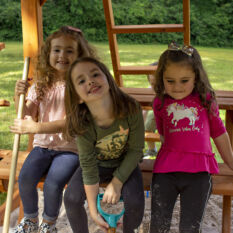 A group of young girls sitting on a GREAT SKYE I SWING SET.