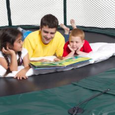 A man and two children reading a book on a Variable Bounce 10 x 17 Ft.