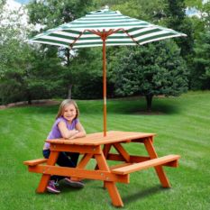 A girl sitting on a Children's Picnic Table with Shade Umbrella.