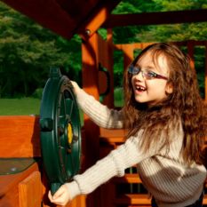 A little girl with glasses playing on a Large Toy Ship's Wheel.