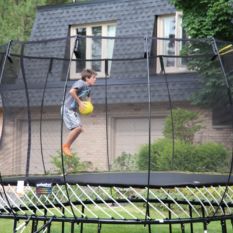 A boy jumping on a SpringFree Large Square Smart Trampoline in a backyard.