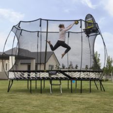 A woman jumping on a SpringFree Large Oval Smart Trampoline in a backyard.