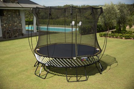 A SpringFree Medium Round Smart Trampoline in a backyard with a net.