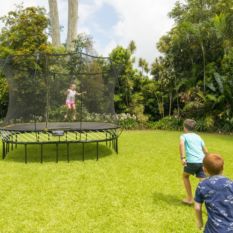 Two children playing on a SpringFree Large Square Smart Trampoline in a backyard.