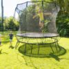Two children jumping on a SpringFree Medium Round Smart Trampoline in a backyard.