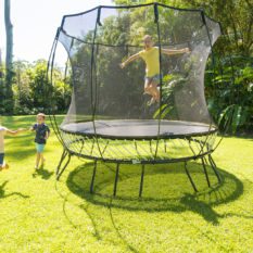 Two children jumping on a SpringFree Medium Round Smart Trampoline in a backyard.