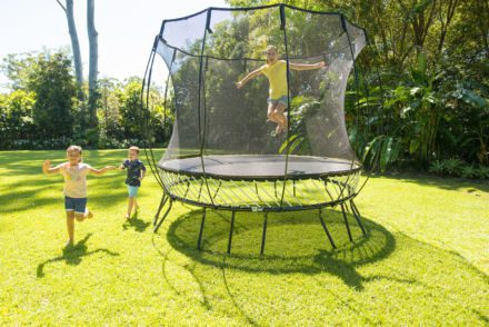 Two children jumping on a SpringFree Medium Round Smart Trampoline in a backyard.