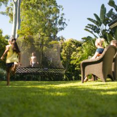 A child is playing with a SpringFree Medium Oval Smart Trampoline in a yard.