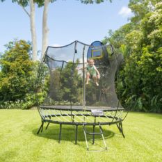 A person jumping on a SpringFree Compact Round Smart Trampoline in a backyard.