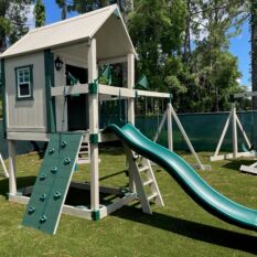 A green Royal Cottage Clubhouse Floor Model with a slide and swings.