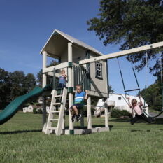 Two children are playing on a VinylNation Royal Cottage Clubhouse in a yard.