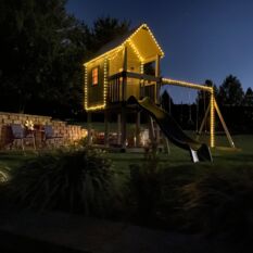 A VinylNation Royal Cottage Clubhouse with lights in the yard at night.