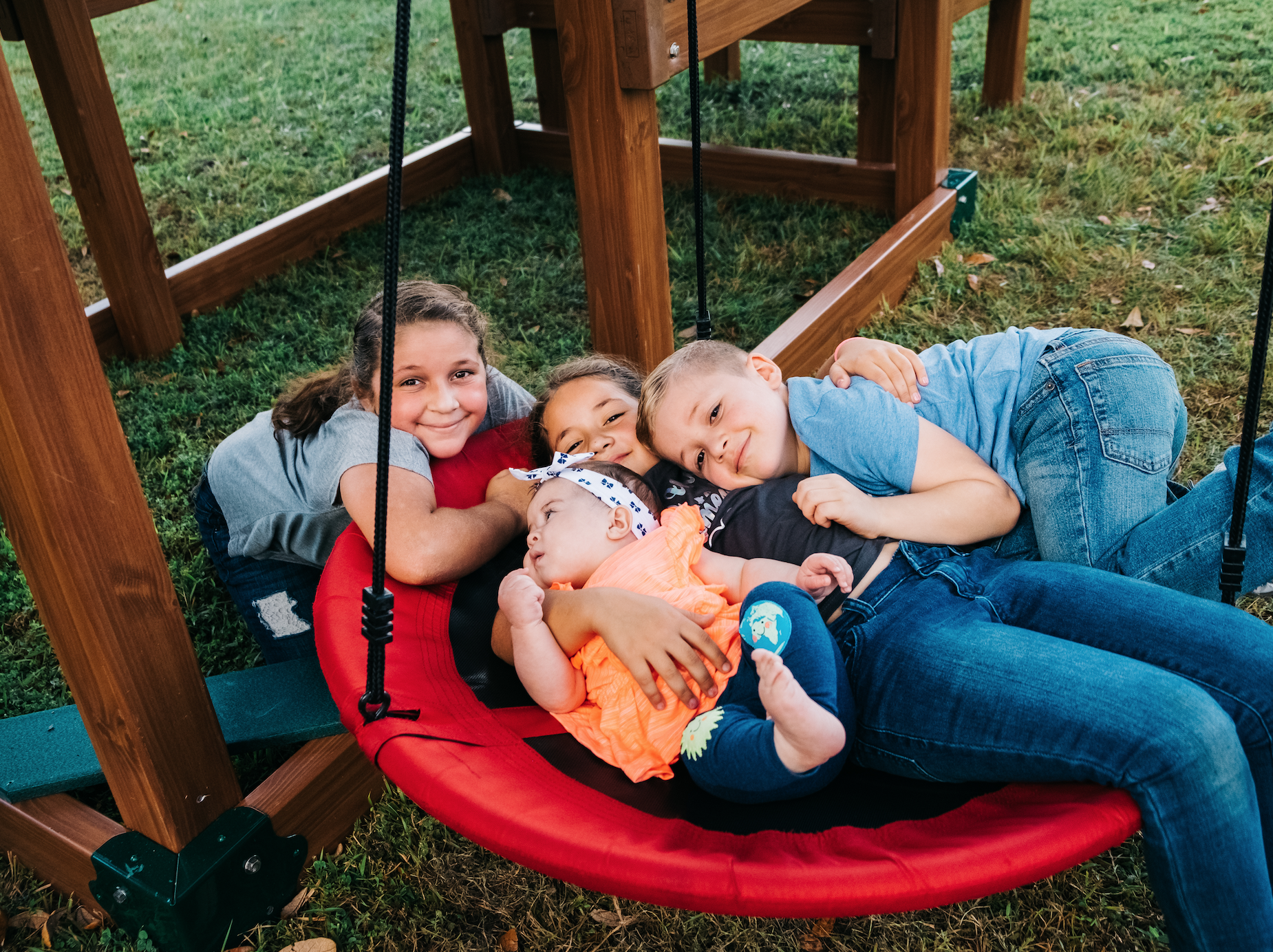 Three children laying on a swing in a playground.