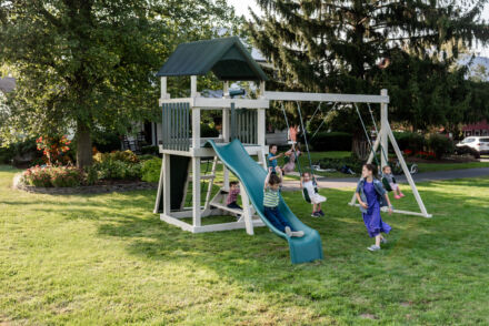 Kids playing on white and blue swing set with a slide